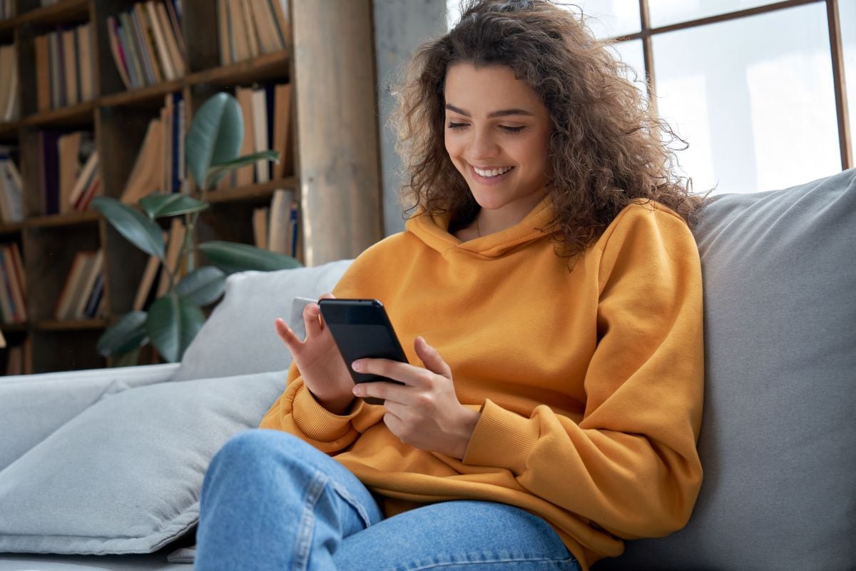 Happy woman checking social media holding smartphone at home